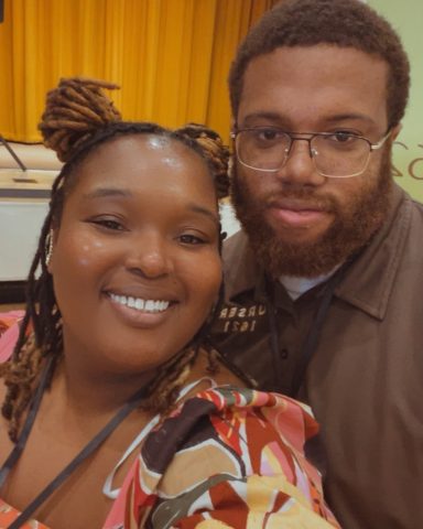 Two smiling individuals posing together with a colorful background.